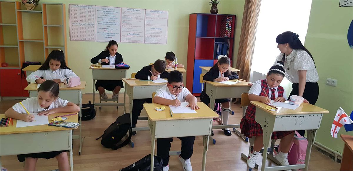 დაწყებითი კლასი წერს, მასწავლებელი მოსწავლეზე დახრილი ეხმარება