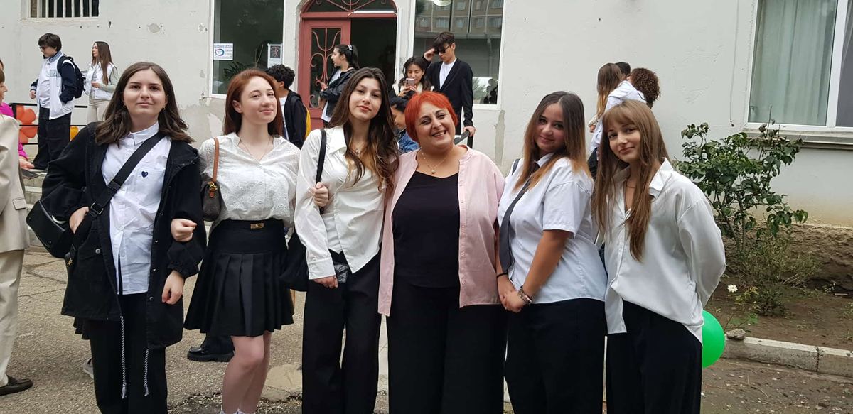 საშუალო საფეხურის მოსწავლე გოგონები მასწავლებელთან ერთად სკოლის შენობის შესასვლელთან